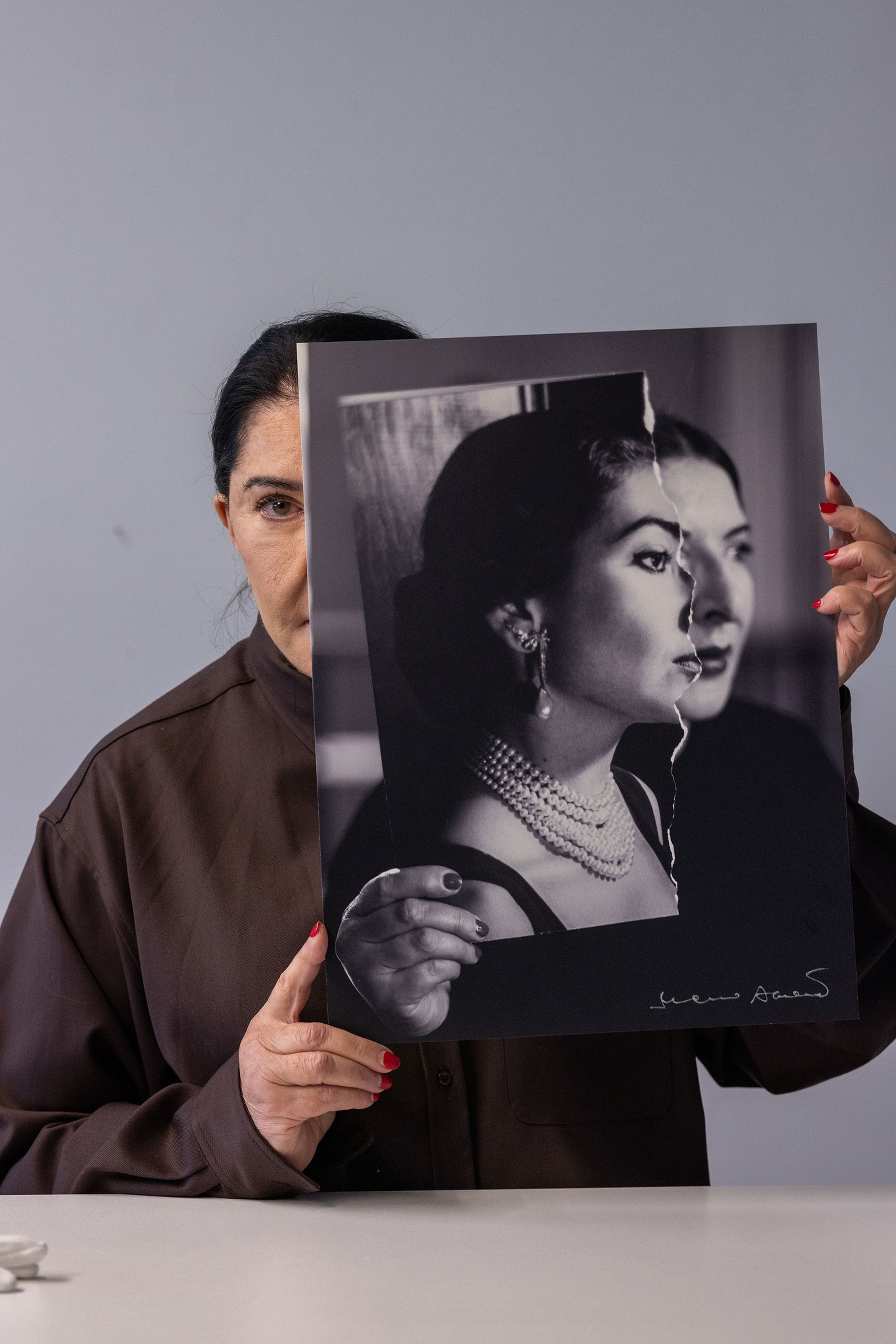 A person holds a torn black-and-white portrait aligned with their face, creating a visual blend of past and present identities. A person holds a torn black-and-white portrait aligned with their face, creating a visual blend of past and present identities.