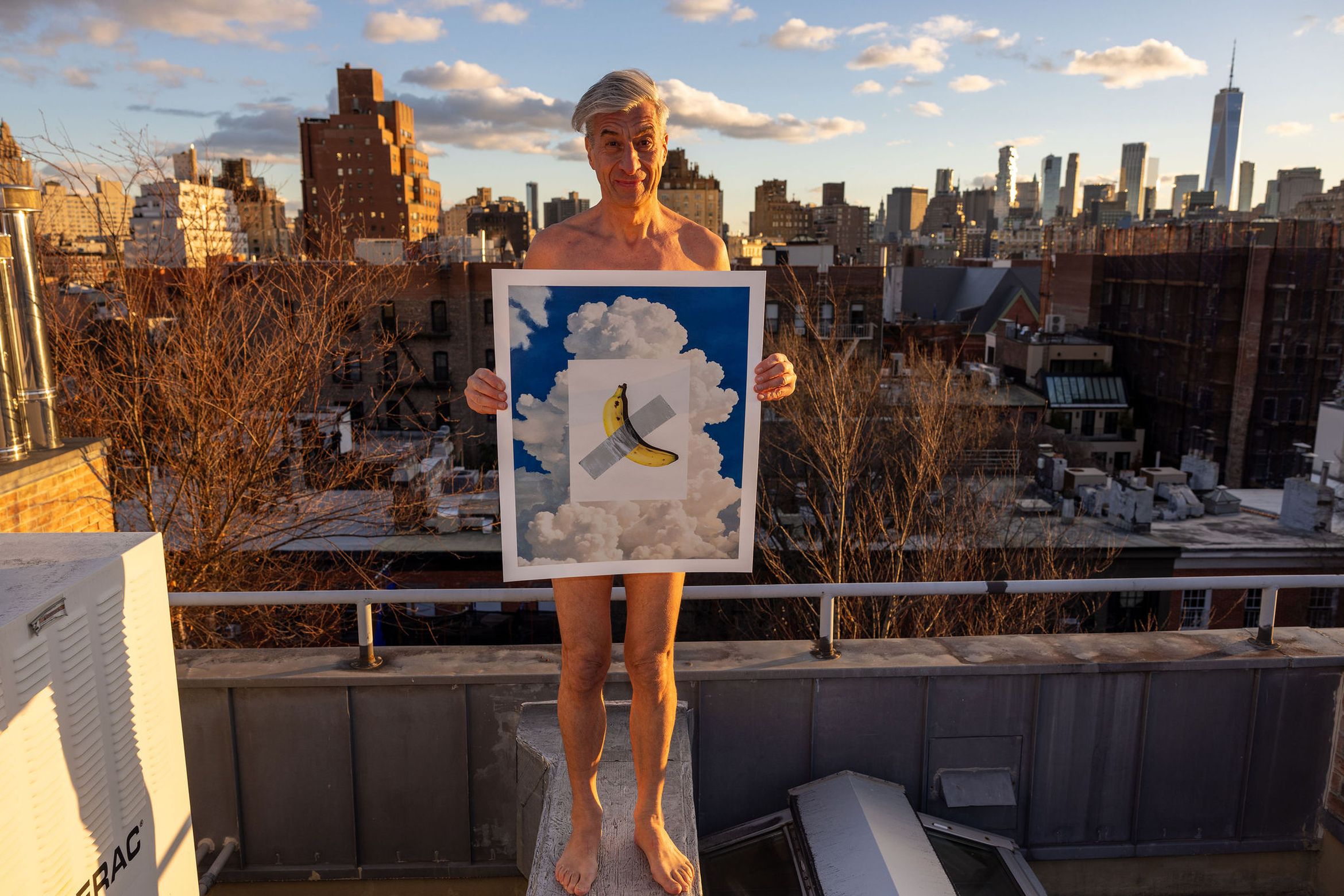 Man standing on a rooftop holding a picture of a banana on a cloudy sky background. City skyline visible in the distance.