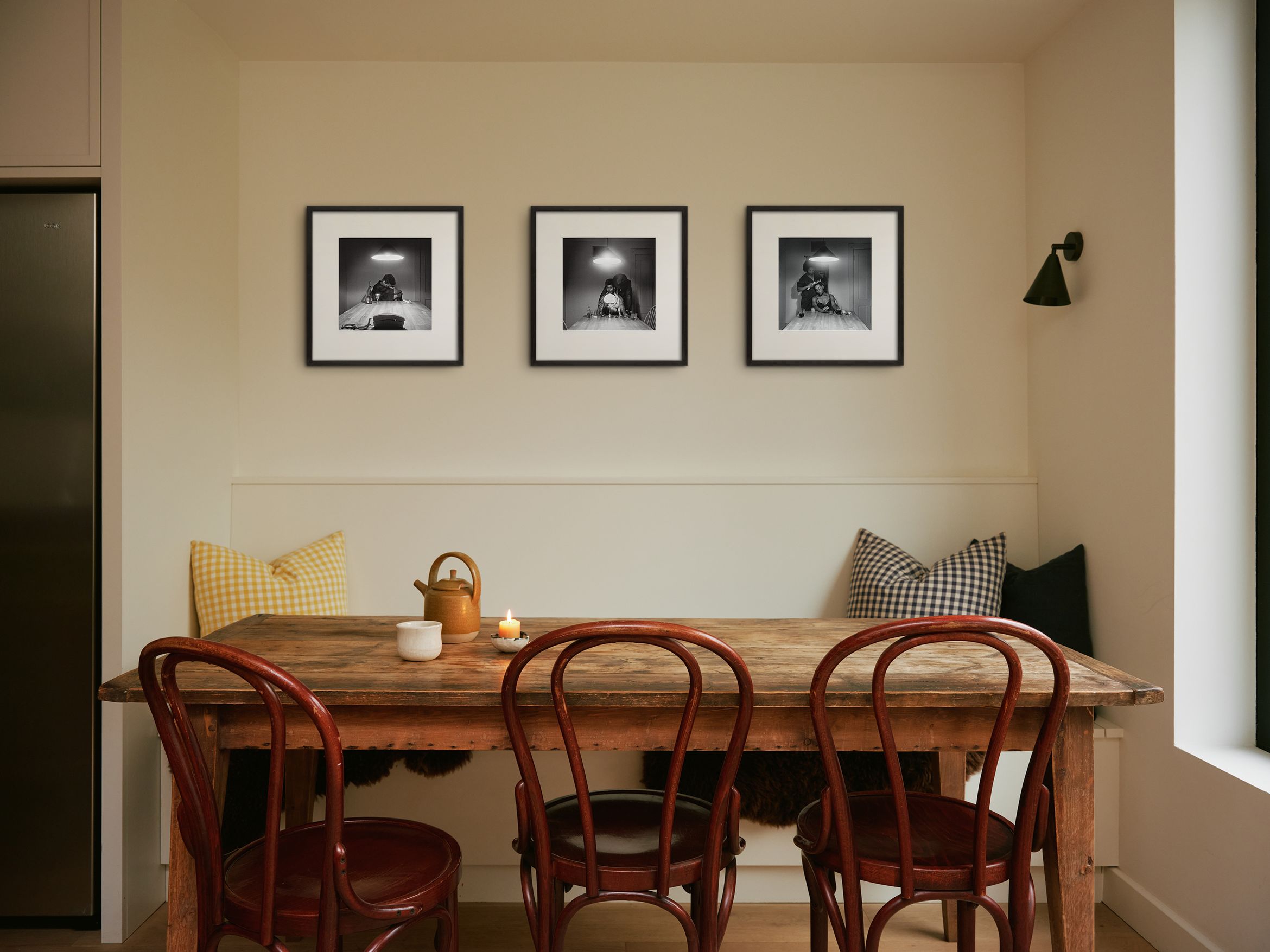 Cozy dining area with a wooden table, four chairs, cushions, a candle, a teapot, and three framed black-and-white photos on the wall. Cozy dining area with a wooden table, four chairs, cushions, a candle, a teapot, and three framed black-and-white photos on the wall.