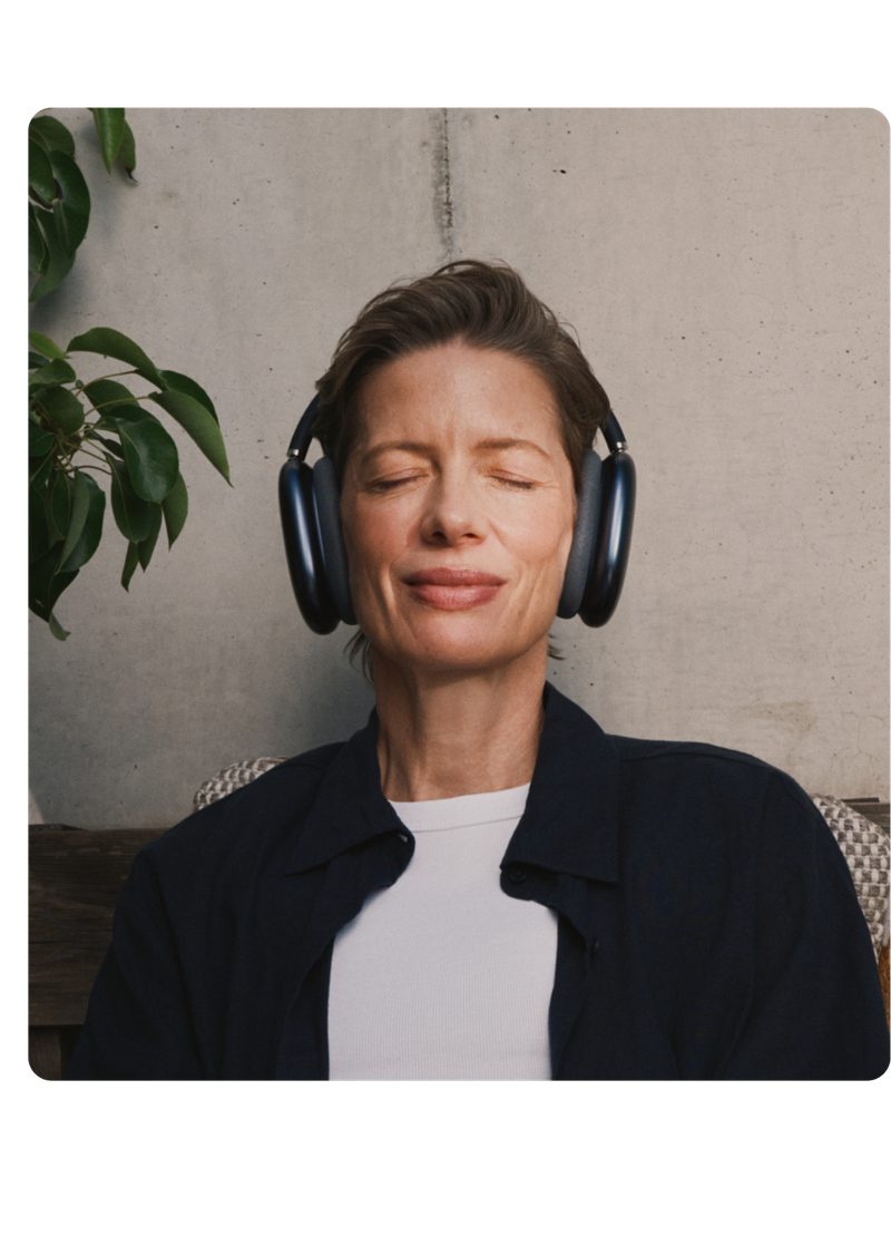 Person sitting with eyes closed, wearing headphones, and leaning against a wall. A leafy plant is visible in the background.