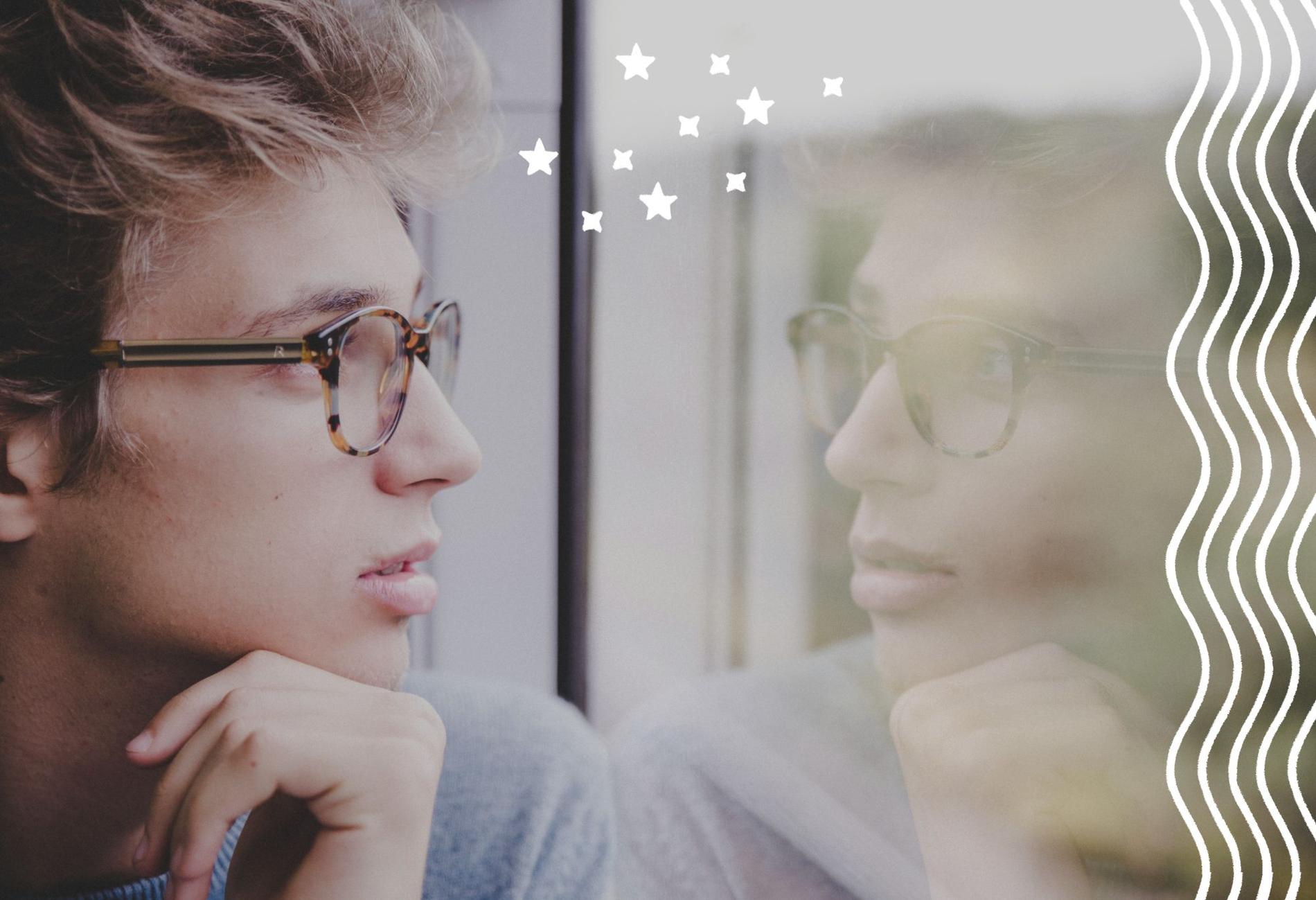 Männlich gelesene Person mit Brille schaut nachdenklich aus dem Fenster.