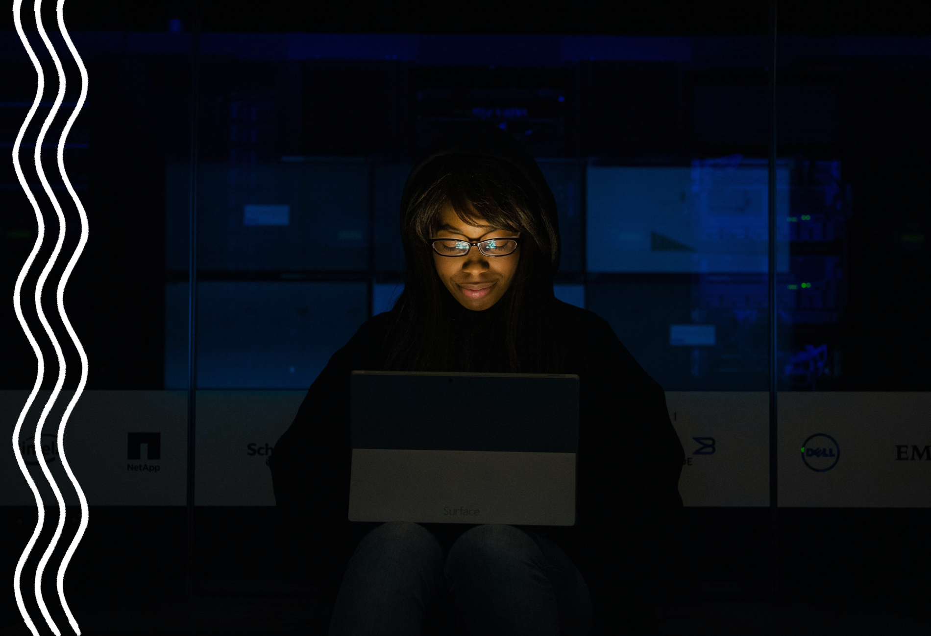 Eine Frau mit Brille sitzt im dunkeln vor ihrem Tablet, dessen Screen in ihr Gesicht leuchtet. Sie sieht konzentriert und zufrieden aus.