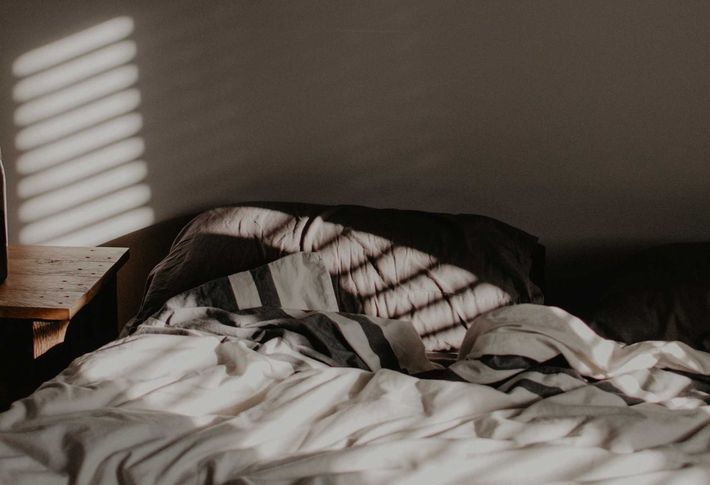 Ein Bett mit dunkelgrauer Bettwäsche wird von mehreren Sonnenstrahlen beleuchtet
