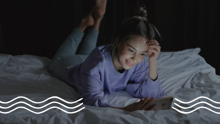 Eine Frau liegt im Dunkeln im Bett und schaut auf ihr Handy, während sie vom blauen Licht des Bildschirms angestrahlt wird.