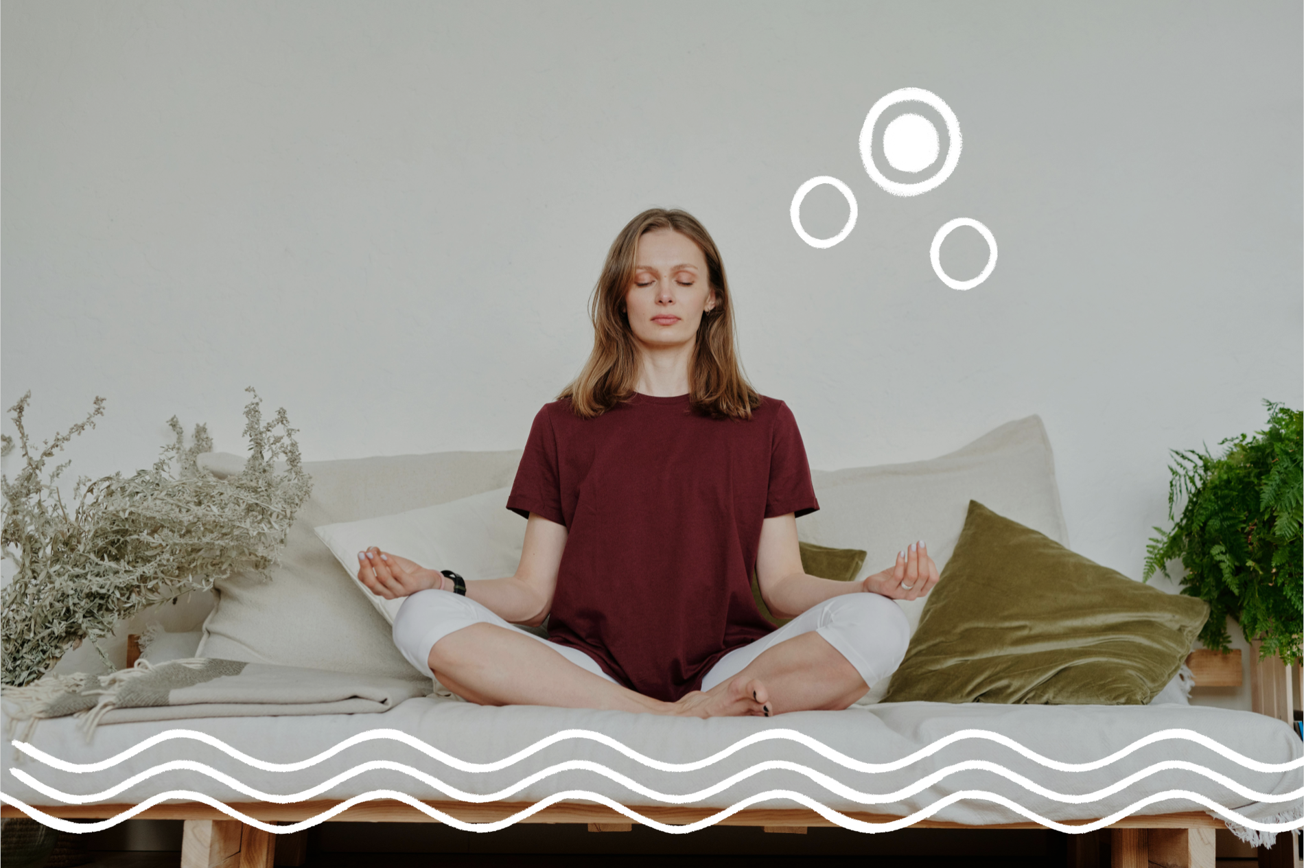 Eine Frau sitzt entspannt in Meditationspose auf einem weißen Sofa. Rechts und links neben ihr stehen Pflanzen, sie ist umgeben von Kissen
