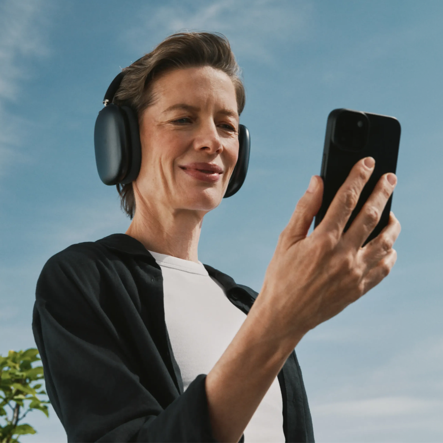 Smiling woman with headphones looking at her smartphone against a blue sky