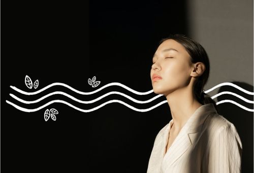 Asiatische Frau mit langen schwarzen Haaren und einer hellen Bluse, die mit geschlossenen Augen das Gesicht in die Sonne streckt.