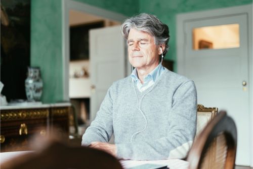 Mann mit grauen Haaren meditiert mit Kopfhörern und geschlossenen Augen