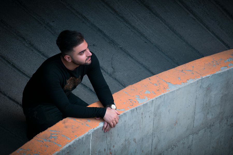 Ein Mann mit dunklen Haaren und schwarzem Oberteil hat seine Arme auf einer Mauer abgelegt und schaut in die Ferne.