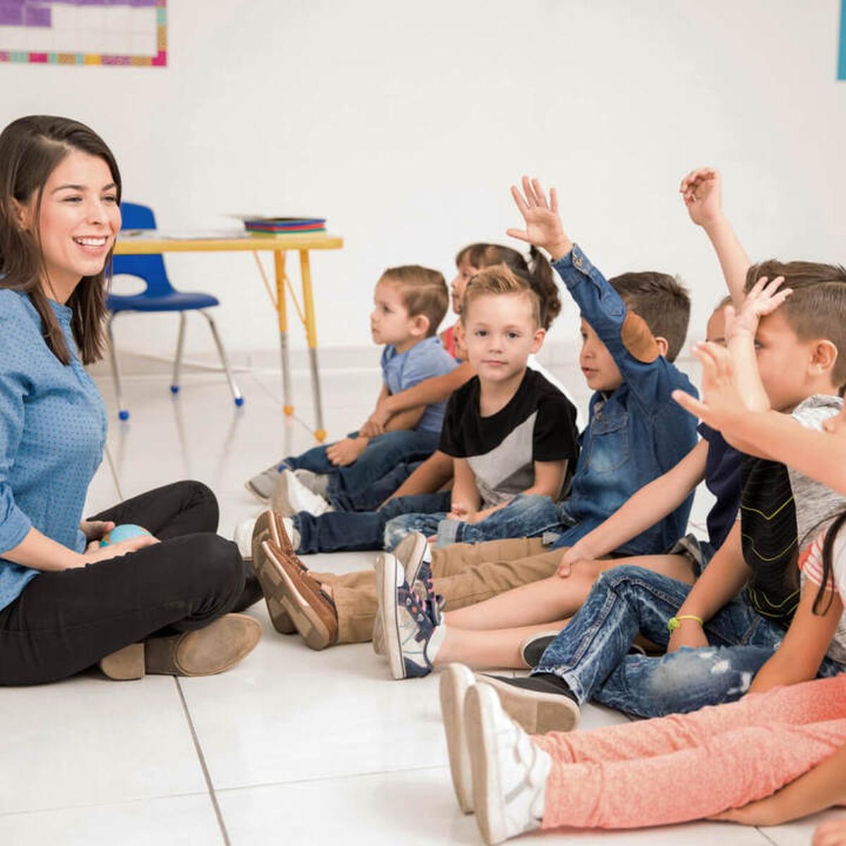 Lehrerin sitzt ihren Schülern lächelnd gegenüber auf dem Boden, bevor alle gemeinsam mit der 7Mind-App meditieren