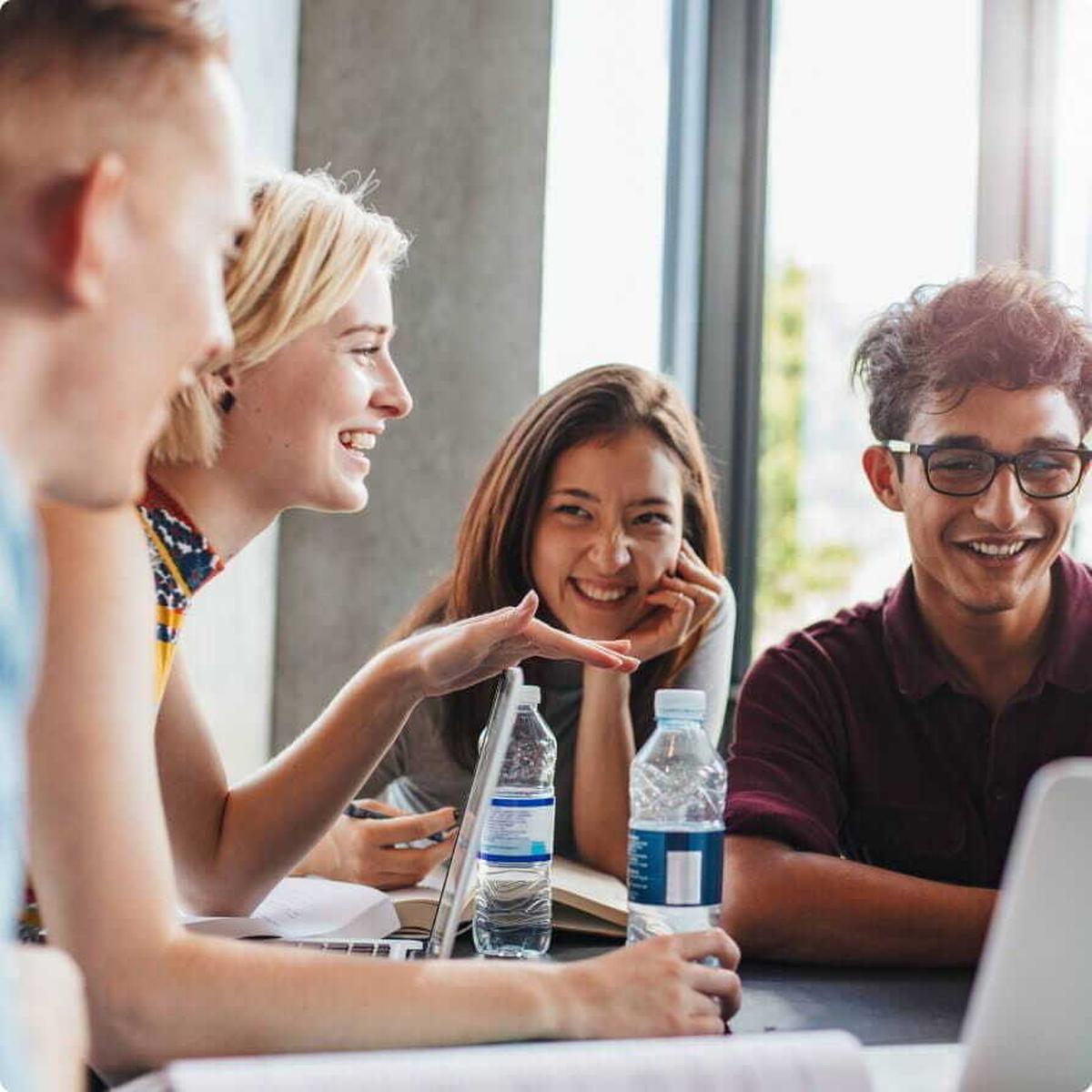 Bild einer Gruppe lächelnder junger Kollegen bei der Gruppenarbeit vor Laptops und Wasserflaschen