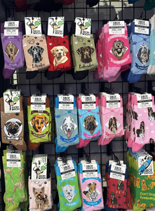 A display of colorful socks featuring various dog breeds, including Labradors, Dachshunds, and Terriers, hanging on a grid wall.