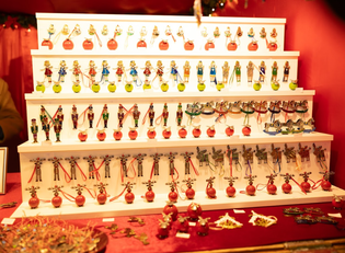 A display of colorful Christmas ornaments, including reindeer, snowmen, and other festive figures, arranged on tiered white shelves.