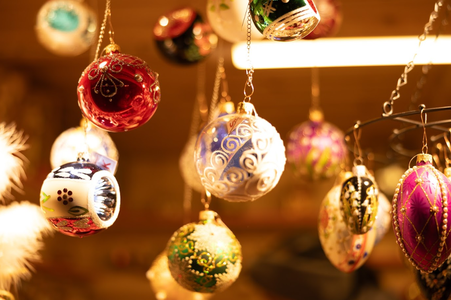 Colorful Christmas ornaments hang against a warm, glowing background. The baubles are intricately decorated, creating a festive, cheerful atmosphere.