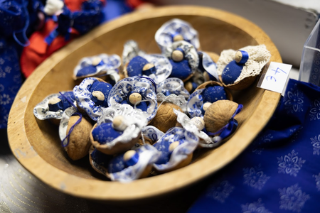 A wooden bowl filled with crafted ornaments resembling tiny sleeping figures in walnut shells, adorned with lace and blue fabric, is priced at 4€.