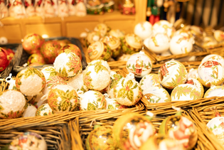 Baskets filled with colorful, decorative Christmas ornaments featuring festive patterns and designs, displayed in a well-lit setting.