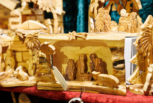 Wooden nativity scene with intricate carvings depicting the Holy Family under a stable, surrounded by palm trees. Warm, rustic, and serene ambiance.