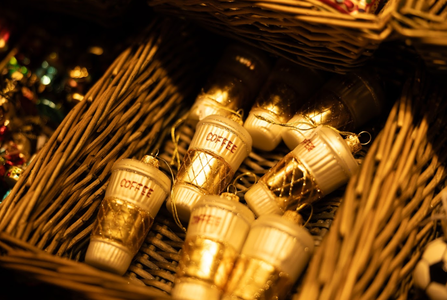 Wicker baskets filled with coffee cup-shaped ornaments, featuring gold accents and the word "COFFEE" written on them.