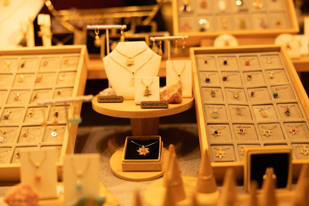 Display of elegant jewelry with gem-adorned necklaces and earrings on stands, labeled "Mondstein" and "Sonnenstein," exuding a warm, luxurious ambiance.
