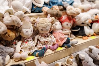 Stuffed dolls with smiling faces and floral dresses are displayed on a store shelf, surrounded by plush animals, creating a cozy and inviting scene.