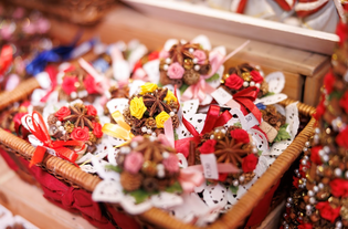 Wicker basket filled with colorful decorative ornaments. The ornaments feature red and yellow flowers, ribbons, and star-shaped accents, creating a festive, cheerful ambiance.