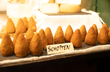 Rows of cone-shaped cheeses labeled "Schotten" on display, with a soft focus background.