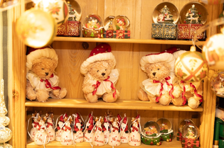 Wooden shelf displaying teddy bears in festive hats, snow globes, and Christmas-themed ornaments.