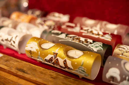 Decorative candle holders in warm tones, featuring winter village scenes with trees and snow. Set on a wooden table with a soft, festive ambiance.