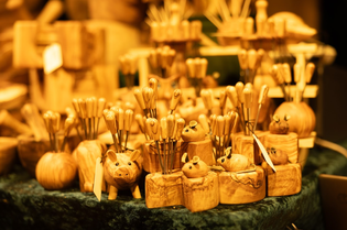 Wooden animal-shaped knife holders with knives displayed on a dark green surface at a craft market.