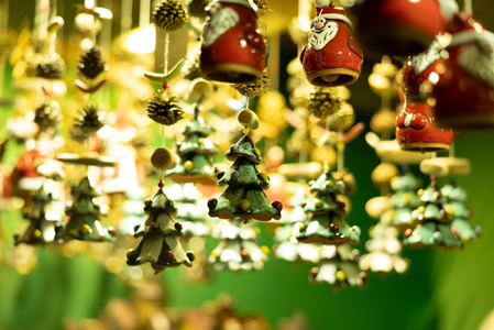 Hanging Christmas ornaments, including small trees and festive figures, with a blurred green background.