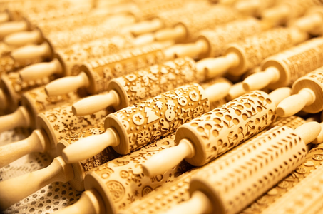 Close-up of intricately patterned wooden rolling pins arranged in rows. Each pin features unique festive designs, creating a warm, artistic atmosphere.