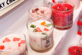 Colorful chunk candles in glass jars, featuring red, pink, and white bases with embedded wax cubes. The scene is vibrant and inviting.