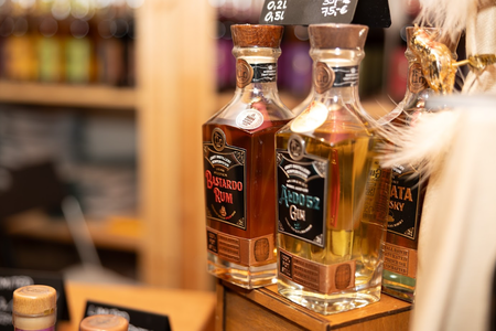 Three bottles of spirits on a wooden shelf, featuring Bastardo Rum and Aldoz Gin. Labels are ornate, with a rustic, warm ambiance in a cozy shop.