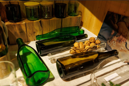 A collection of green and brown glass bottles and jars on a wooden shelf, alongside walnuts. The scene conveys a rustic, cozy ambiance.