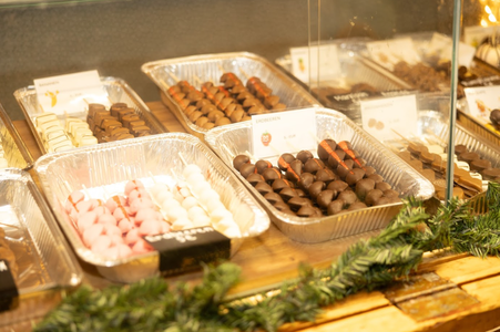 Assorted chocolate covered fruits displayed in trays behind a glass case, with festive greenery in the foreground.