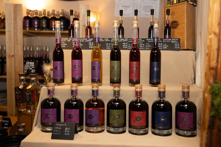 A display of various colorful liquor bottles arranged in tiers on a beige cloth. Each bottle has a vibrant label, with signs listing prices and details. Warm, inviting ambiance.