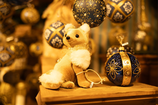 A plush fox toy sits on a wooden surface surrounded by ornate blue and gold Christmas ornaments.