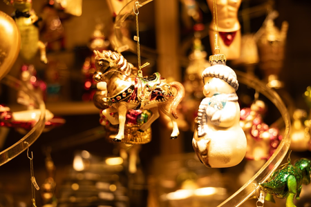 Close-up of festive ornaments, including a decorated rocking horse and a snowman, hanging in warm lighting, creating a cozy holiday atmosphere.