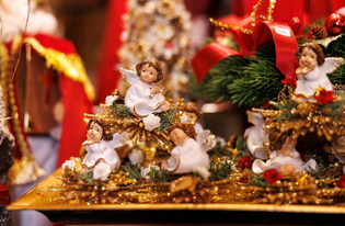 Ceramic angel figurines with wings sit on a glistening gold base adorned with white flowers and red bows, creating a festive, joyful atmosphere.