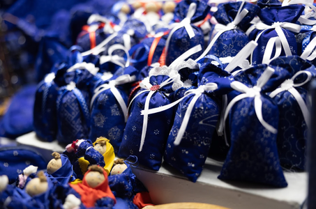A collection of small blue fabric bags tied with white ribbons, featuring intricate patterns. In front, tiny handcrafted dolls in vibrant clothing are displayed. The scene conveys a festive, artisanal vibe.