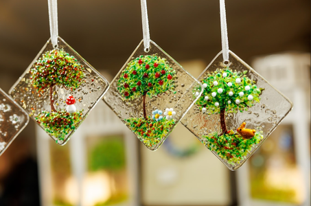 Three glass suncatchers hang, each depicting a colorful tree with textured leaves and apples, framed by clear glass squares. The mood is whimsical and bright.