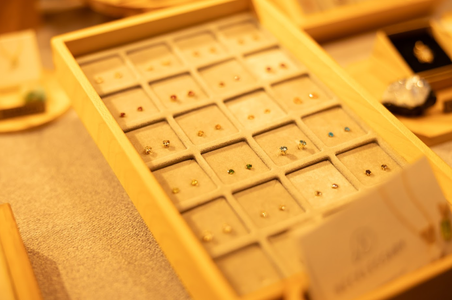 A warm-toned display of colorful stud earrings in a wooden jewelry tray, each neatly arranged in individual slots, creating an elegant, inviting atmosphere.