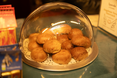 A tray of round pastries under a glass dome on a counter, with warm lighting highlighting their golden-brown crusts.