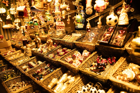 A festive market stall displaying a variety of colorful Christmas ornaments and decorations in wicker baskets under warm lighting.