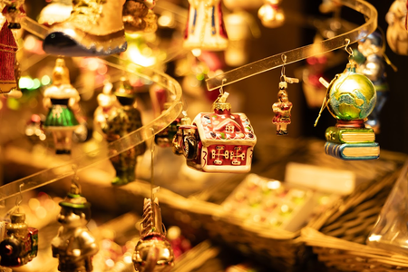 Close-up of festive Christmas ornaments, including a red house, globe on books, and various figurines, hanging on a spiral display. Warm lighting.