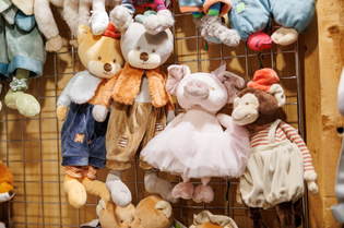 Plush animal toys hang on a grid display, including a fox in overalls, a bear in an orange jacket, a pig in a tutu, and a monkey. Warm, cozy ambiance.