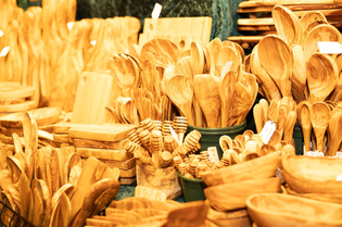 A variety of wooden kitchen utensils, including spoons, cutting boards, and honey dippers, displayed in a market setting.