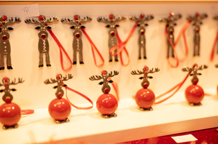 Rows of reindeer ornaments with red noses and red spherical bases, each with a red ribbon, displayed on a shelf.