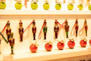 Rows of colorful nutcracker ornaments and red apple-shaped decorations displayed on white shelves.