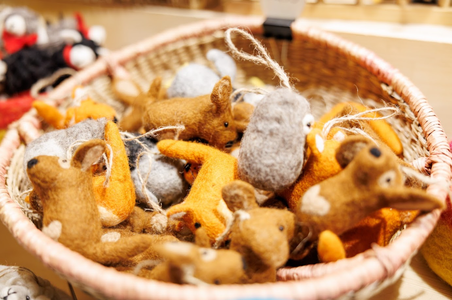 A basket filled with small, colorful felt animal toys, including brown and orange deer and gray mice. The scene is warm and playful, evoking a cozy, handmade feel.